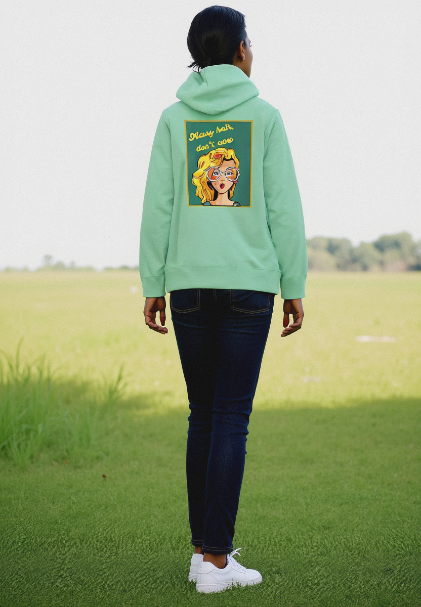 A person standing with their back towards the camera wearing a green hoodie with a text and graphic design, in an open field.