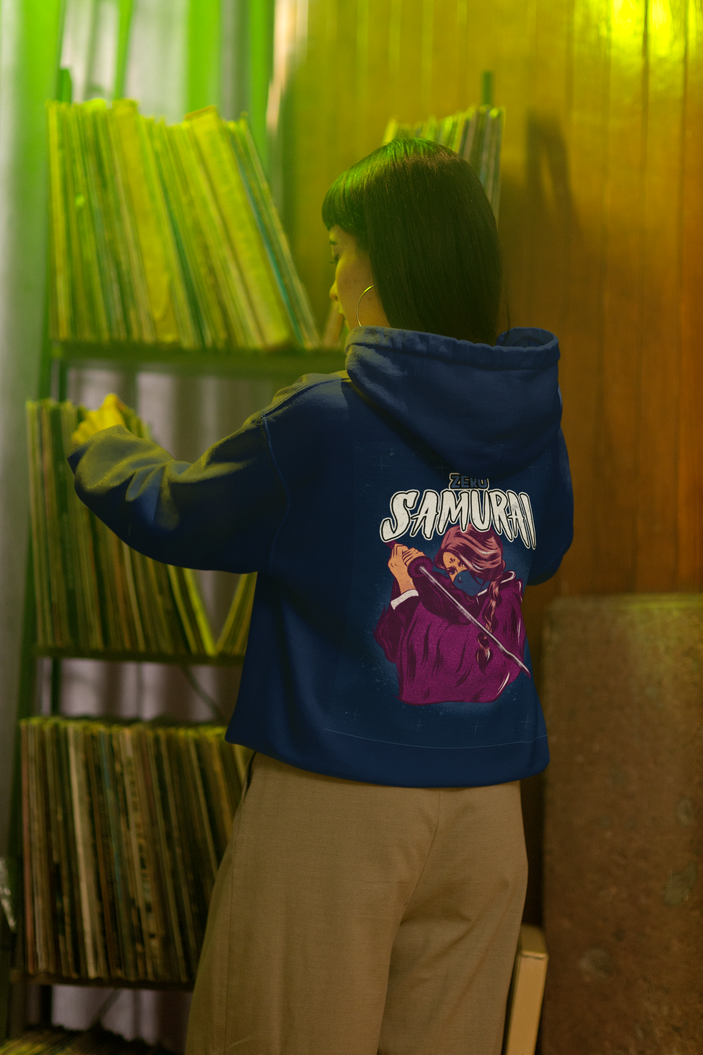 A person wearing a blue hoodie with 'SAMURAI' written on the back in large letters, standing in a room with bookshelves.