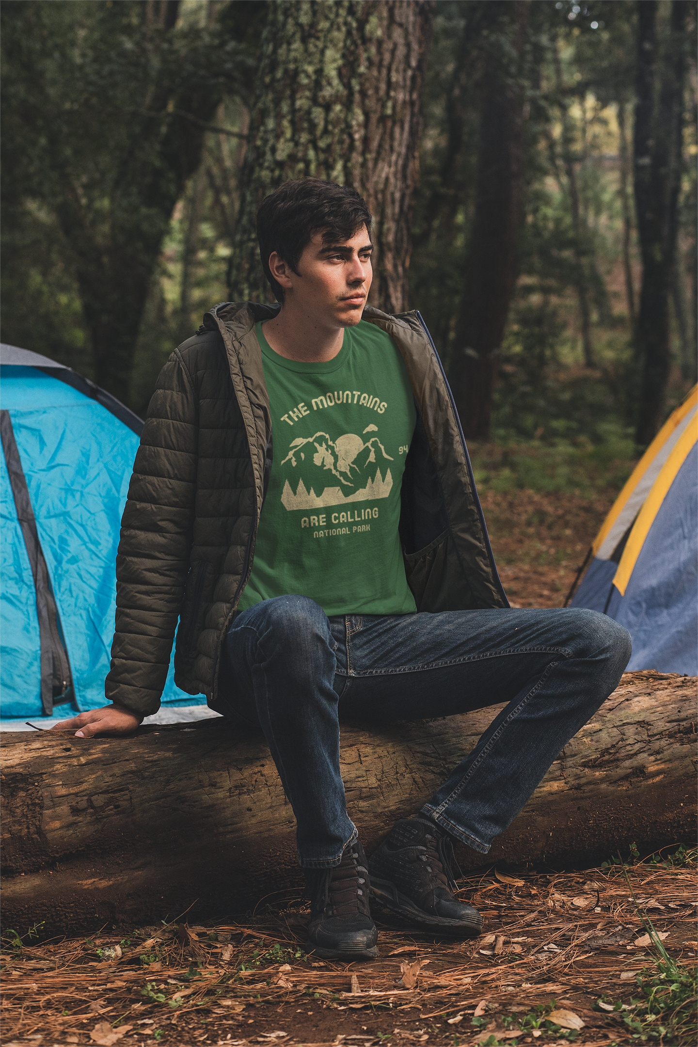 Person sitting with t shirt on a log in a forest with camping tents in the background