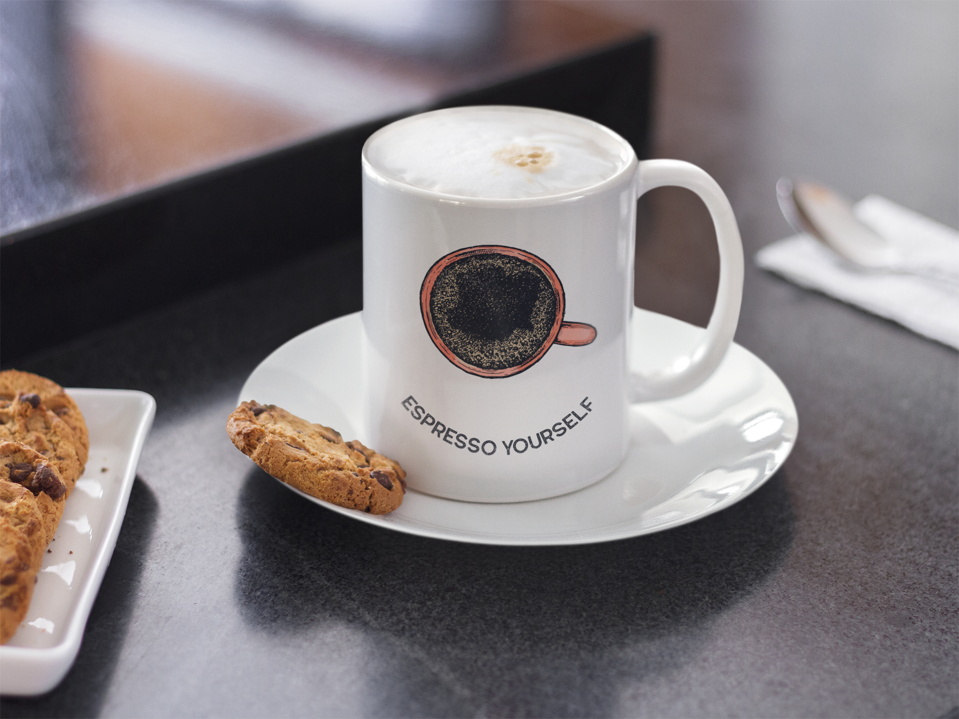 A white ceramic mug with 'ESPRESSO YOURSELF' text and a coffee bean graphic on the front, accompanied by a saucer and a cookie, placed on a black surface.