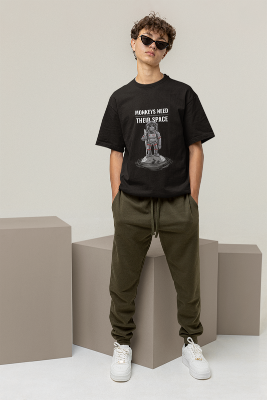 A person wearing a black oversized t-shirt with a graphic and text, paired with green joggers and white sneakers.