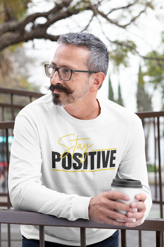 Man wearing a white sweatshirt with 'Stay Positive' text, holding a coffee cup outdoors.