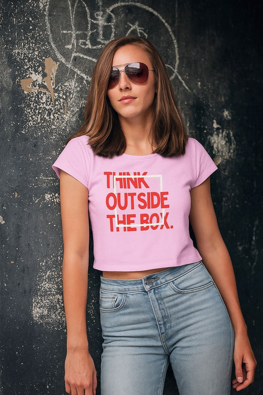 Woman wearing a pink t-shirt with 'Think Outside The Box' text against a dark textured wall.