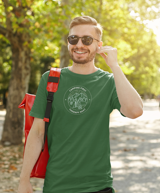 Man wearing a green t-shirt with a logo and text, standing outdoors with trees in the background.