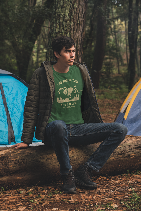 Person sitting with t shirt on a log in a forest with camping tents in the background